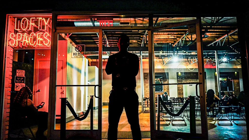 A silhouetted figure standing inside a neon-lit storefront at night.