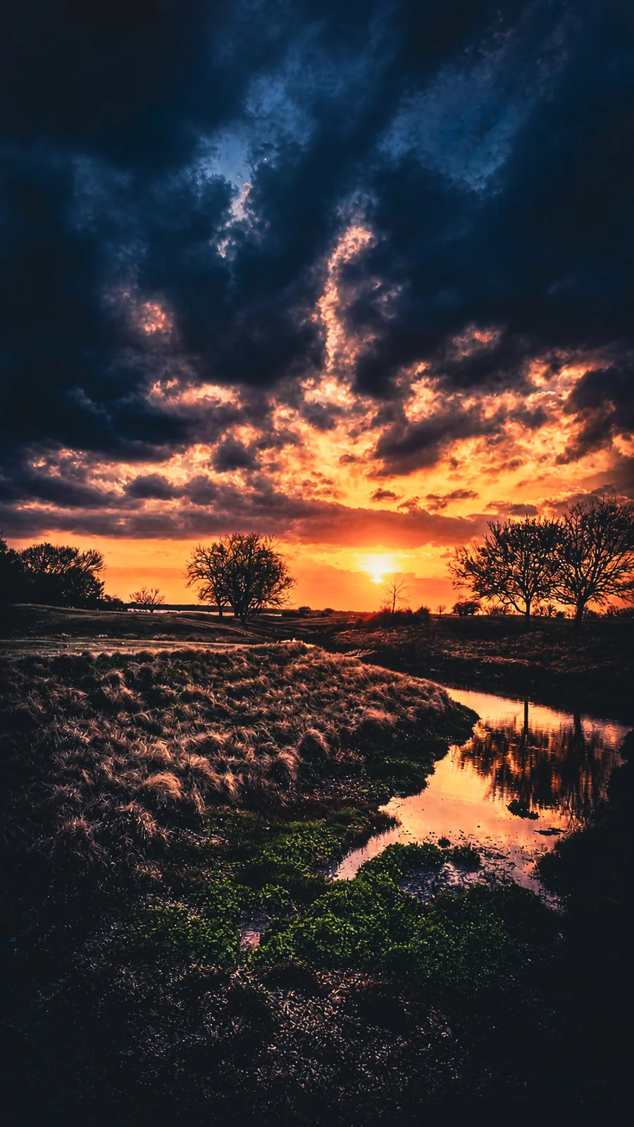 A dramatic sunset spreading across an open landscape beneath textured clouds.