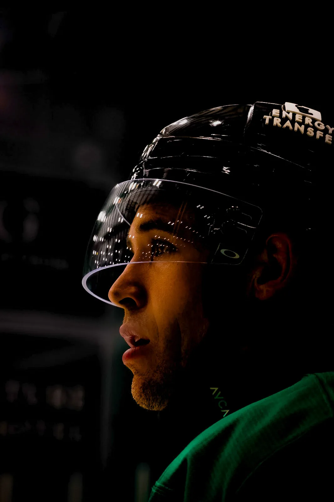 Close profile of a hockey player wearing a helmet under arena lights.